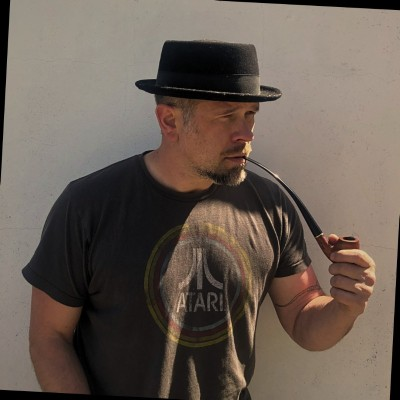 Kevin Lint in a black pork-pie hat and Atari T-shirt, holding a pipe